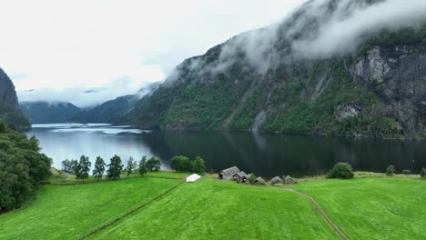 idyllic morning at bolstadfjorden sea in norway - old boathouses at shoreline and misty tall mountains in the fjord - slow sideways moving aerial establishing scene