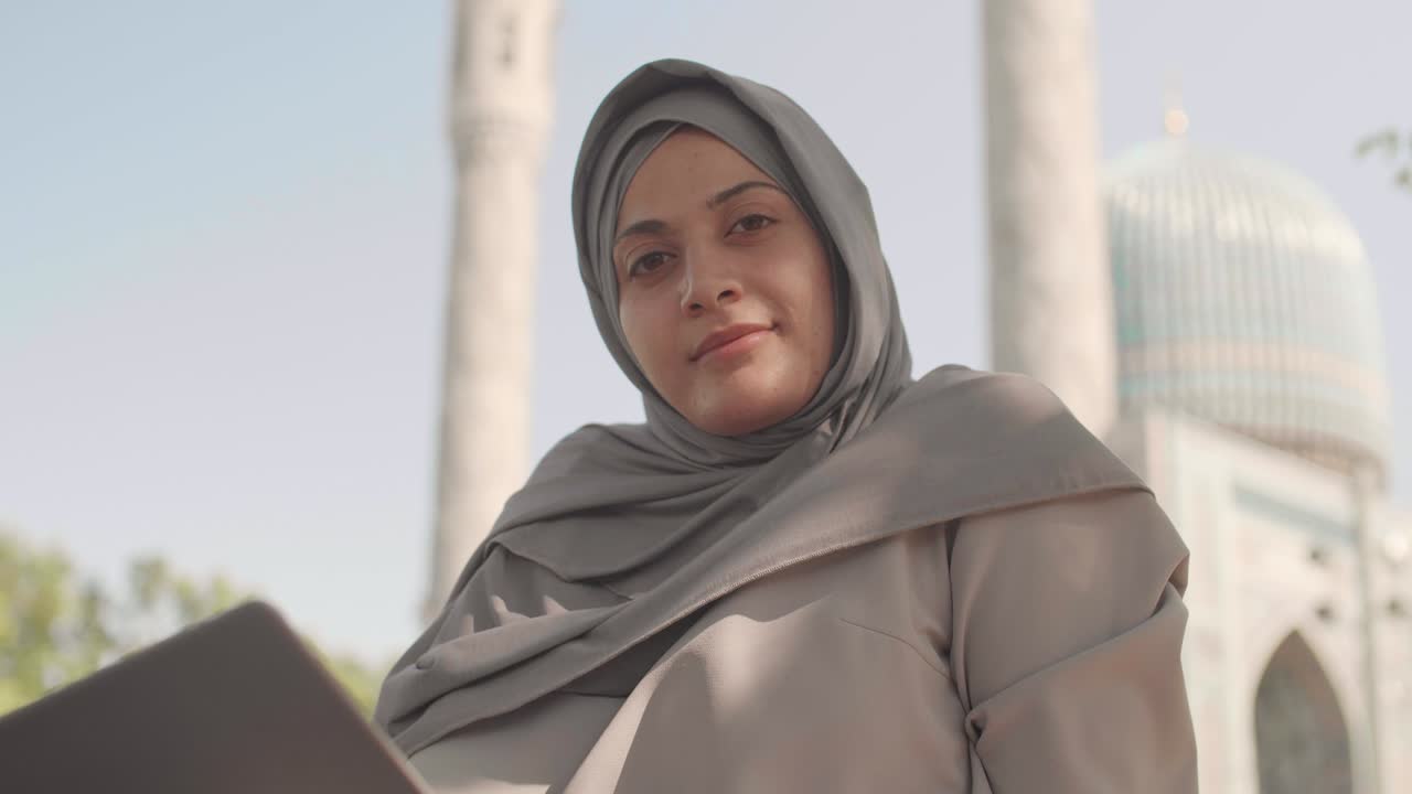 retrato de una mujer musulmana con una computadora portátil cerca de una mezquita