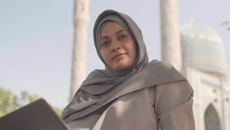 portrait of muslim woman with laptop near mosque