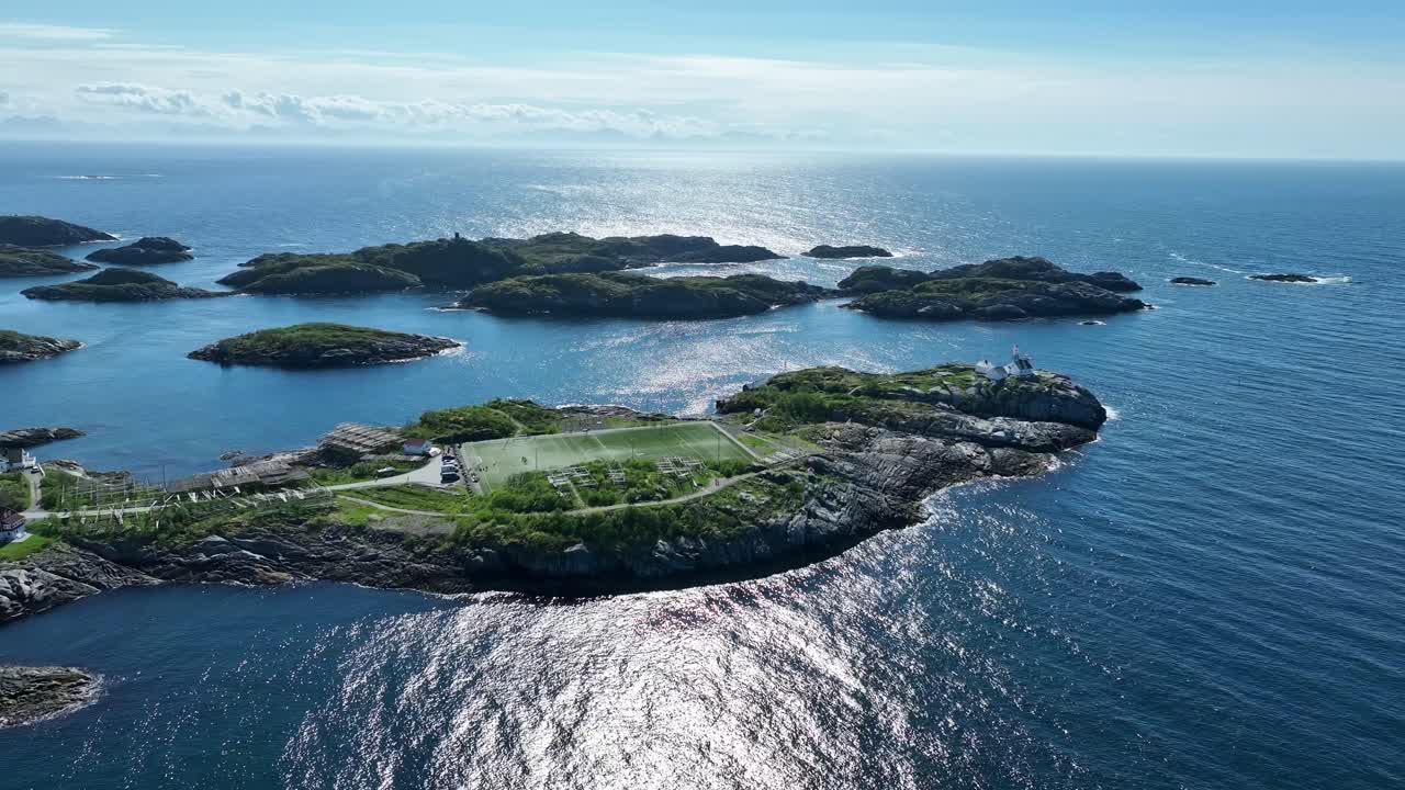 Side aerial of iconic soccer field Henningsvaer Stadium, Lofoten, Norway in North Sea, drying racks for stockfish around pitch