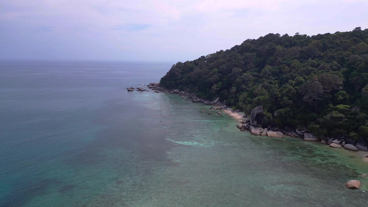 Turquoise water gently washing a sandy beach surrounded by granite rocks and lush tropical vegetation. Dramatic aerial view flight panorama overview drone