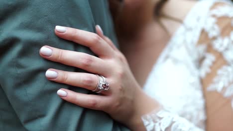 close up of wedding ring on finger of bride holding grooms arm