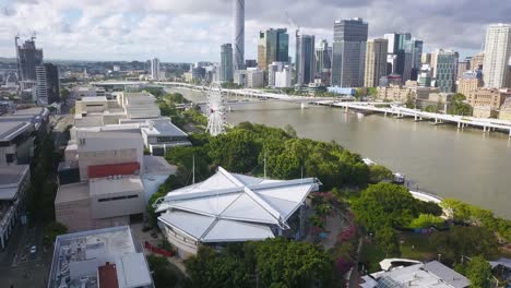 Vuelo-Aéreo-Hacia-Atrás-Desde-Los-Parques-De-South-Bank,-Brisbane-CBD-En-Segundo-Plano