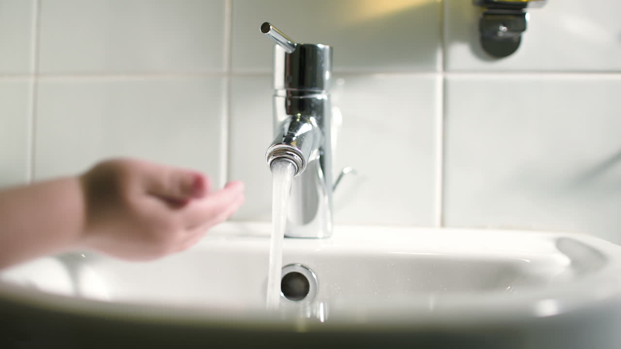 Mano di bambino che tocca l'acqua che scorre dal rubinetto