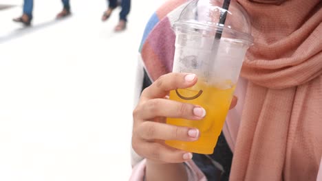 a woman drinks orange juice with ice from a plastic cup with a straw