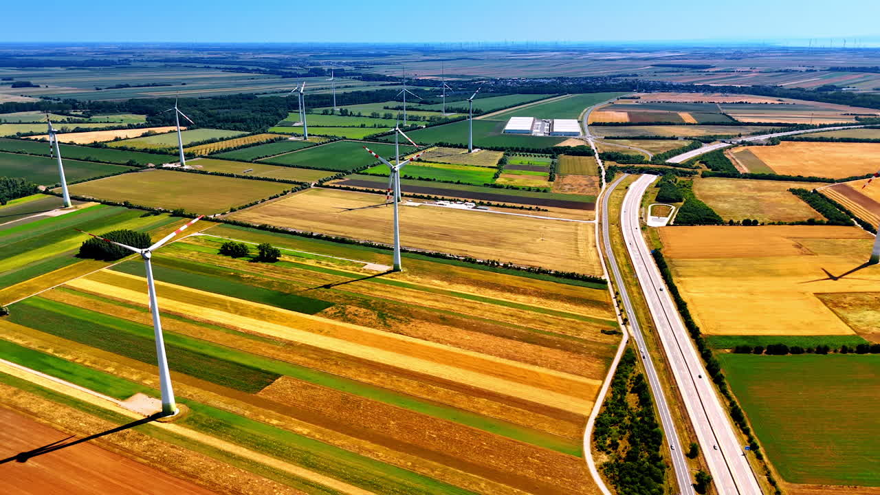 Green, yellow and brown patches of fields in the picturesque countryside. Wind turbines stand still on a windless day. Aerial view