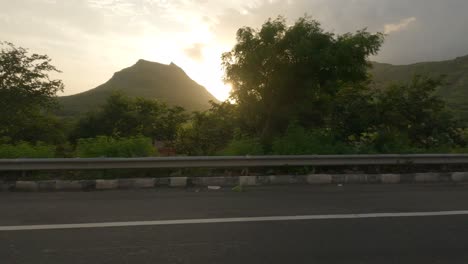 side view of a car driving on a highway in maharashtra looking at the beautiful sunset on a sahyadri mountain landscape