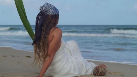 Mujer-Joven-Con-Un-Vestido-Blanco-De-Playa-Se-Sienta-En-La-Arena-Mientras-Observa-Las-Olas-Del-Océano