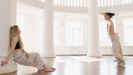 male dancer training in the studio while her female co worker looking at him leaning on a column