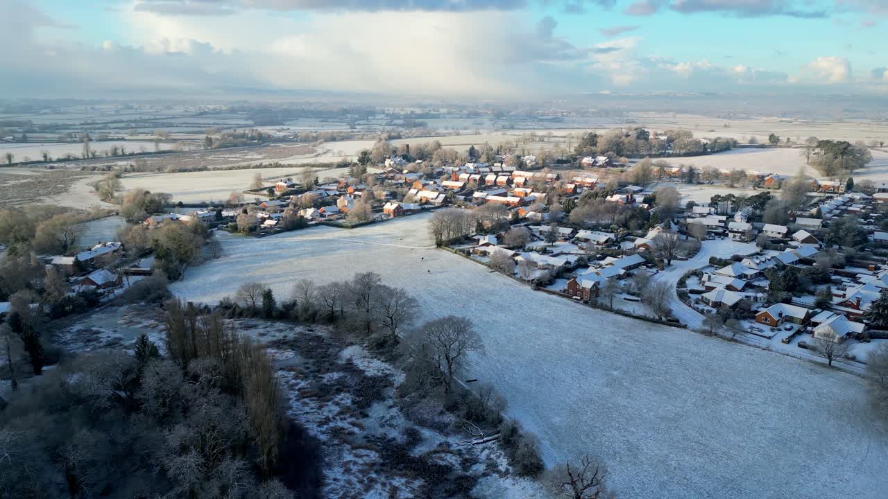 The sun rises over a snow-covered English village, casting a golden glow over rooftops and icy country lanes.
