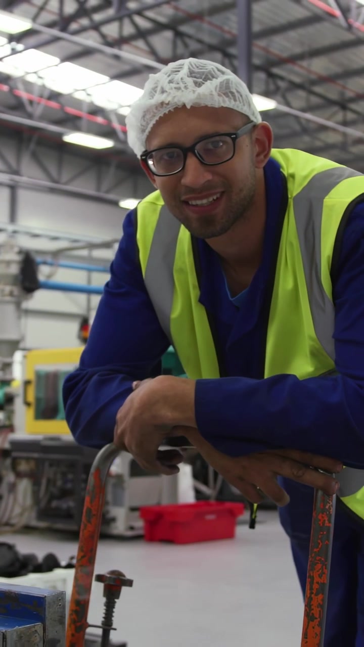 Vertical video: Plant worker leaning on pallet truck digits causing adjusting grip smiling at data