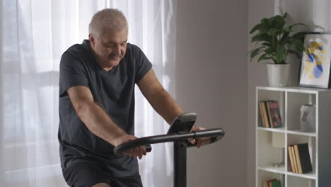 Preocuparse-Por-La-Salud-Y-Perder-Peso-El-Hombre-De-Mediana-Edad-Está-Entrenando-Solo-En-Casa-En-Bicicleta-Estática-Buena-Condición-Física