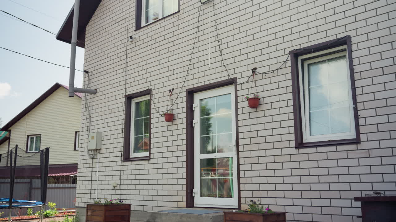 Mother Helps Child, Lady In Pink Supports Child Navigating Garden Steps And Play Zone, Woman Dressed In Pastel Guides Young Child Across Garden Steps Into Cozy House Amid Playful Surroundings