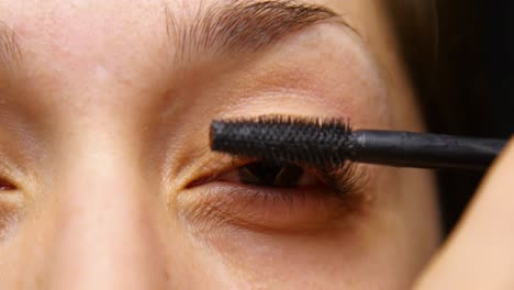 woman applies mascara to her eye lashes