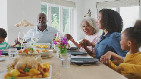 Familie-Mit-Mehreren-Generationen,-Die-Zu-Hause-Am-Tisch-Händchen-Hält-Und-Gnade-Sagt,-Bevor-Sie-Gemeinsam-Isst