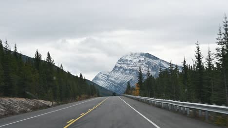 road trip with car driving on the road and rocky mountains on overcast day