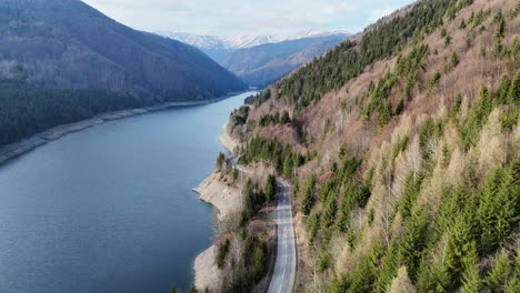 A-winding-road-along-a-tranquil-lake-surrounded-by-forested-mountains