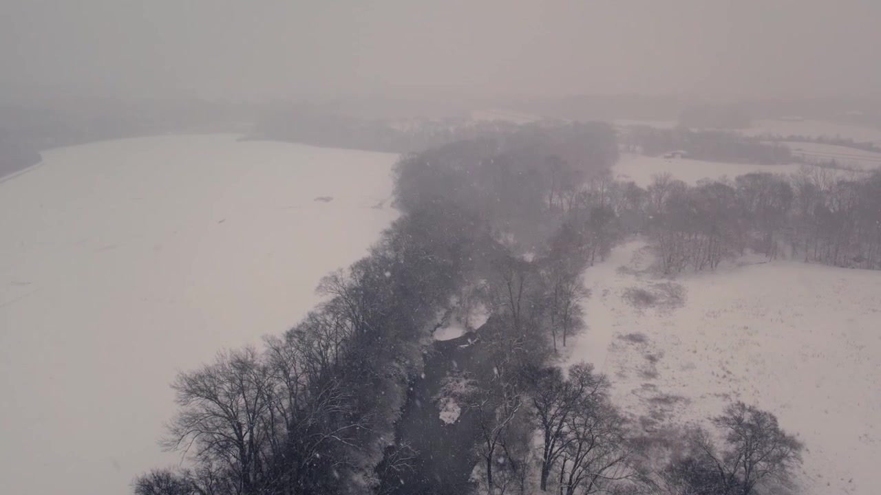 Luftaufnahme eines Flusses, der bei Schneefall durch eine schneebedeckte Landschaft strömt