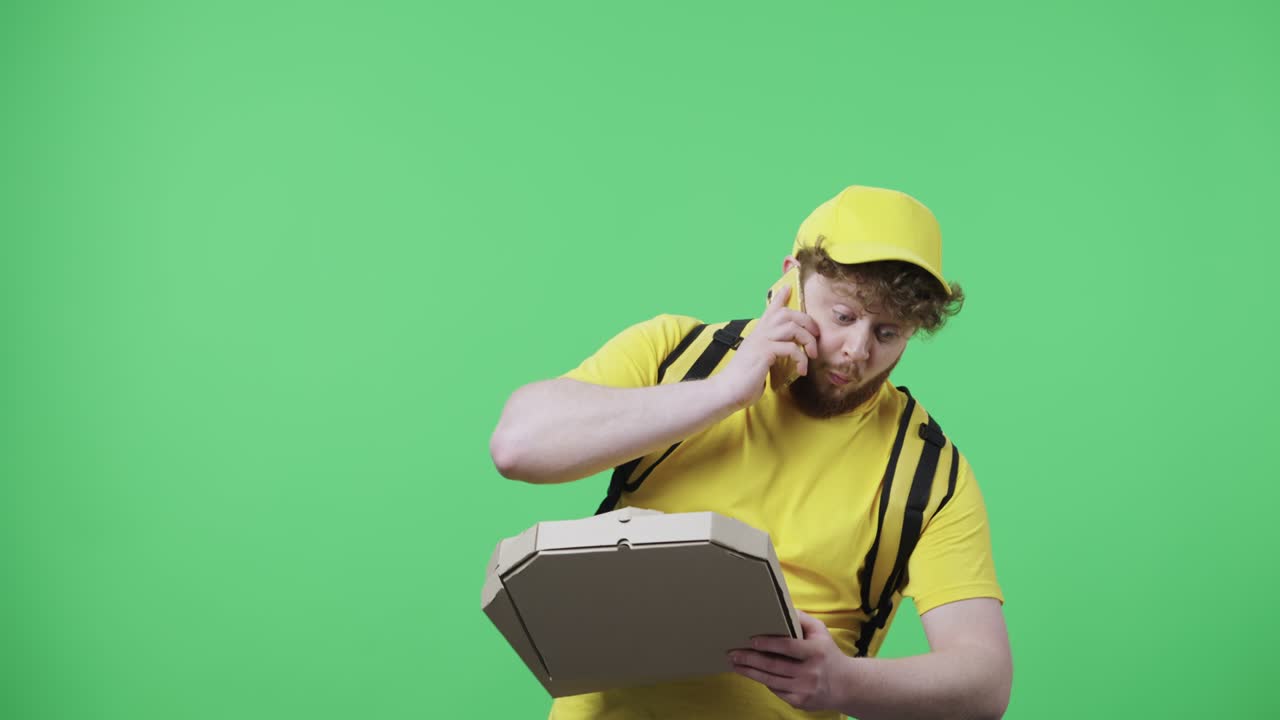 전화로 대화하는 젊은 남성의 초상화 피자 상자를 떨어뜨리고 매우 화가 납니다. 녹색 화면에 포즈를 취하는 테르모 가방과 함께 노란색 배달 택배 유니폼을 입은 은 머리 남성 59.97fps