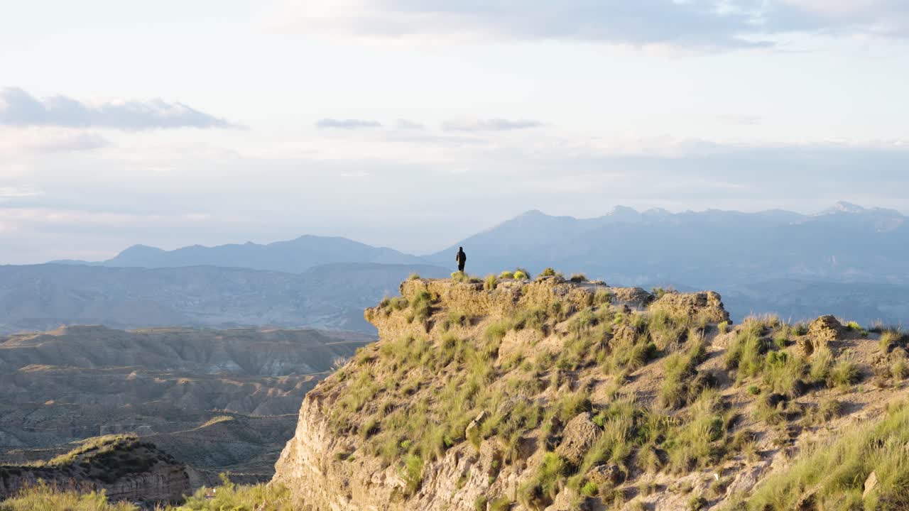 Lone man standing on rocky cliff with vast valley view at sunset