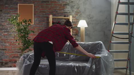 Mujer-Mide-La-Longitud-Del-Sofá-Cubierto-Con-Papel-De-Aluminio-En-La-Sala-De-Estar