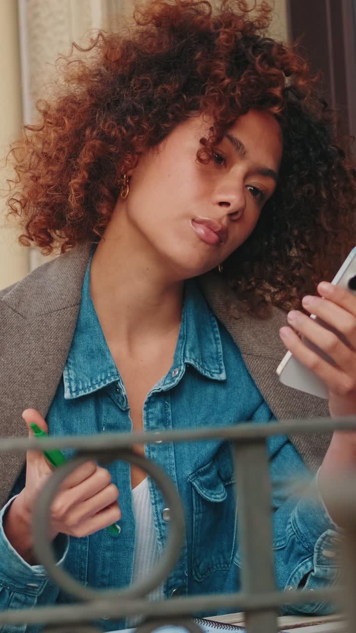 Giovane donna con capelli ricci che usa lo smartphone all'aperto