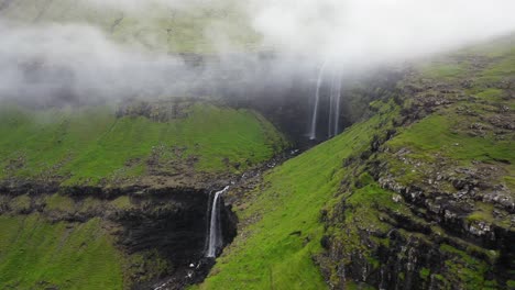 Fossá-Waterfall,-reveal-behind-cliffs-and-mist-in-Faroe-Islands,-aerial-pan