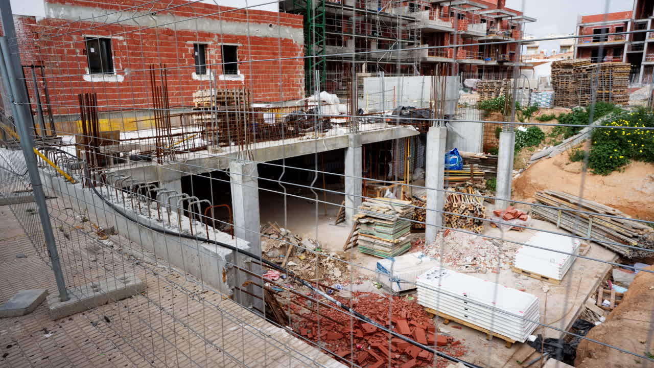 Desarrollo residencial activo mostrando una estructura sin terminar con pilares de hormigón, paredes de ladrillo, andamios y materiales en un solar urbano durante la construcción de viviendas modernas.