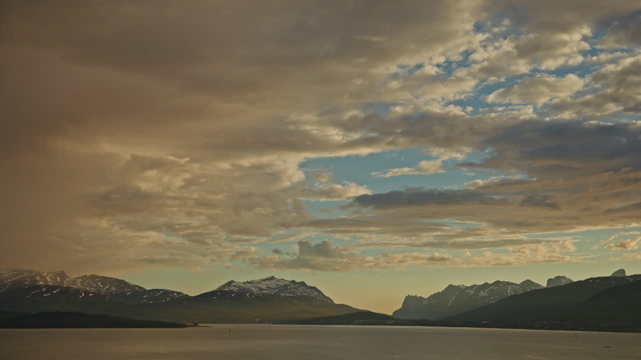 Midnight sunset over the Norwegian Fjords in Tromso.
Arctic golden hour twilight over the snowy mountains and traveling clouds. Picturesque nordic landscape.