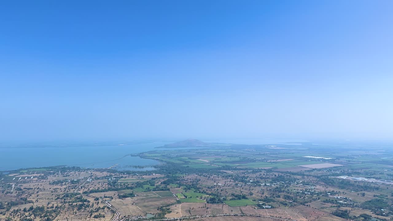 Pemandangan panorama lambat dari puncak bukit pedesaan Lopburi, waduk, dan patung Buddha di bawah cahaya siang yang cerah