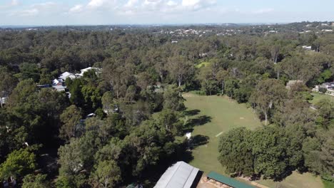 Drone-ascending-over-country-sheds-to-reveal-a-green-field-and-a-country-town-in-the-background