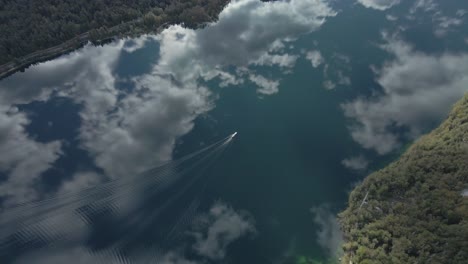 Nubes-Y-Cielo-Que-Se-Reflejan-En-La-Superficie-De-Agua-Suave-Del-Lago-Con-Un-Barco-Que-Crea-Ondas,-Antena