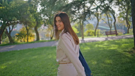 una chica serena disfruta de un paseo por el parque iluminado por el sol inmersa en la contemplación de la vista de atrás.