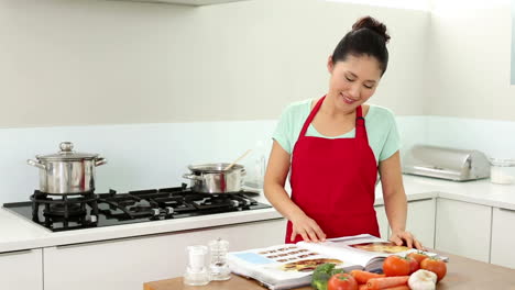 mujer sonriente preparando la cena y consultando su libro de recetas