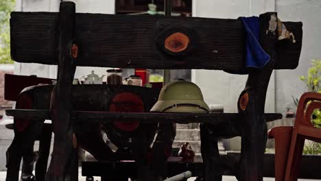 rustic outdoor tea setup in vietnam, featuring a green pith helmet on a wooden bench, with a teapot, jars, and a pot of roll tobacco on a wooden table. vintage, tranquil atmosphere with natural wooden