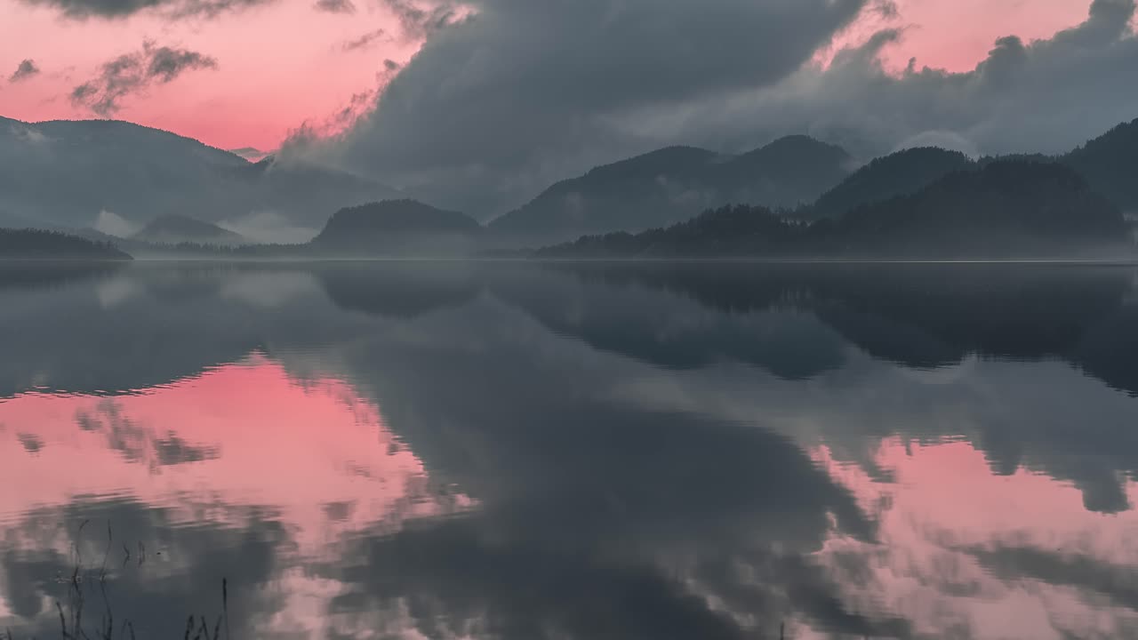 극적인 분홍색 해가 지는 하늘과 어두운 폭풍우 구름이 조용한 물에 반사되어 다른 세상의 광경을 만니다.