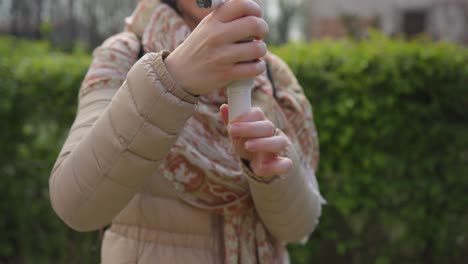 mujer con abrigo de crema jugando extendiendo el agarre en el gimbal de mano para el teléfono inteligente afuera