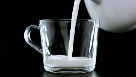 vierte la leche en una taza transparente sobre un fondo negro. cierra.