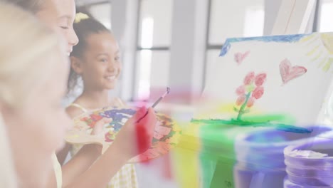 Animation-of-paint-pots-over-happy-diverse-schoolgirls-painting-in-art-class