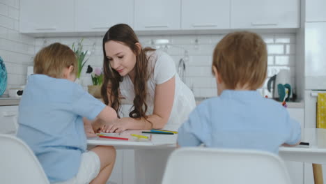 a young woman helps kids to paint standing in the kitchen