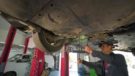 young car mechanic at repair service station inspecting car wheel and suspension detail of lifted automobile. bottom view.