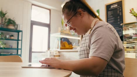 Mujer-Caucásica-Con-Síndrome-De-Down-Navegando-Por-Una-Tableta-Digital-Mientras-Está-Sentada-En-Un-Café