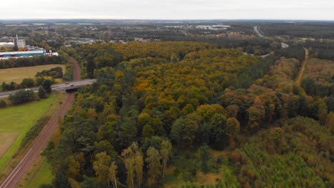 Thetford-forest-with-railway-track-and-road-at-Brandon,-England---aerial-drone-flying-backward-shot