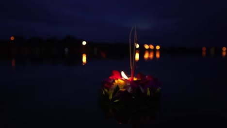 festival loy krathong: gran y hermoso krathong con una vela encendida e incienso encima hecho de hojas de plátano y flores naranjas en el agua azul oscuro por la noche