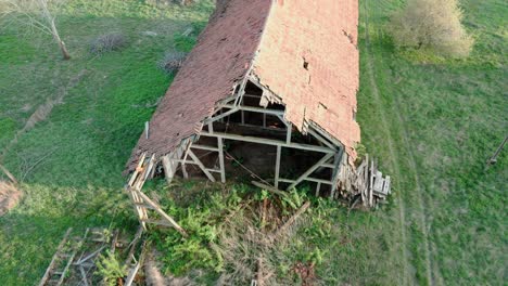 Decaying-outbuilding-with-red-roof-tiles-against-green-grass-in-the-background