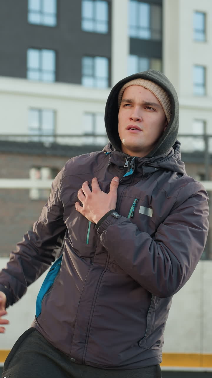 спортсмен настраивает куртку, протягивая руки в подготовке к спортивной практике на современной городской спортивной арене на фоне высоких жилых зданий и головных столбов