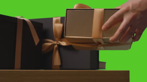 close up of man picking up gift wrapped presents in boxes decorated with ribbon on table shot against green screen 2