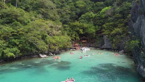 tourists kayaking in tropical emerald cadlao lagoon, el nido, karst rock formations at island, philippines, aerial view