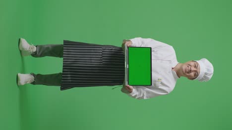 full body of asian man chef smiling and showing green screen laptop to the camera while standing in the green screen background studio