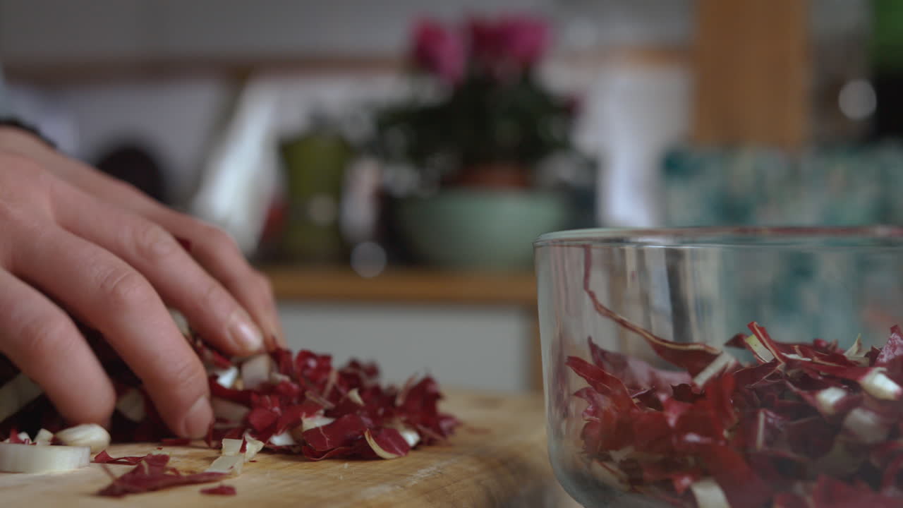 부엌에 있는 나무 판자에 다진 이탈리아 치커리로 유리 도시락을 천천히 채우는 팬 여성의 손을 닫으세요